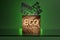 Greenwashing concept. A wooden box with the inscription eco and harmful additives E are poured into it. Green background.