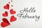 Greeting card with text Hello February. Red paper hearts on white wooden background, flat lay