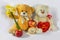 A greeting composition with a pair of funny teddy bear characters with a red heart, a bouquet of daffodils and ripe red apples on