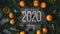 Greeting inscription Happy New year 2020 on a wooden background with a frame of tangerines and fir branches