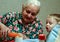 A Gret grand-mother pouring carrot dring into the glass for little boy standing by the table, blur and grain effect.