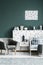 Grey armchair, bedside table, metal bed and dotted wall decorations in a dark green bedroom interior