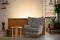Grey armchair next to wooden table in living room interior with plants and light. Real photo