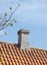 Grey brick chimney designed on slate roof of house building outside against blue sky background. Construction of