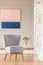 Grey chair next to table with flowers in elegant living room interior with pastel painting. Real photo