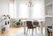 Grey chairs at table under gold lamp in living room interior with windows and plants. Real photo