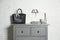 Grey chest of drawers with bag, books and decor elements near brick wall