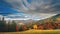 Grey clouds float over coloured mixed forests covering hills