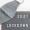 Grey colored Flatlay letter board with message text lockdown 2021 and protective face mask. Lock down loading concept