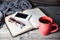 Grey cozy knitted scarf with cup of coffee or tea, phone, glasses and open book on a wooden table.