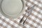 Grey empty plate with vintage fork and knife on beige checkered tablecloth.