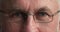 Grey eyes of elderly man looking at camera through glasses