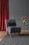 Grey floral chair with black cushion standing on dark carpet in elegant room interior with fresh tulips on gold metal table and re