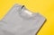 Grey folded t-shirt with blank tag for your design isolated on yellow background.