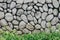 Grey or gray stone wall with natural texture round stone with low bush in the front. Natural stone old style wall.