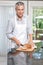 Grey hair man cutting bread in apron