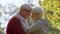 grey-haired married couple touching with their heads and hugging, nature background medium closeup