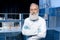 Grey haired scientist in lab coat looking at camera with arms crossed