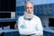 Grey haired scientist in lab coat looking at camera with arms crossed