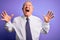 Grey haired senior business elegant man standing over purple isolated background crazy and mad shouting and yelling with