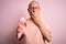 Grey haired senior man holding breast cancer awareness pink ribbon over pink background cover mouth with hand shocked with shame