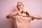 Grey haired senior man wearing glasses standing over pink isolated background smiling in love showing heart symbol and shape with