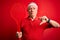 Grey haired senior tennis player man holding racket over red isolated background with angry face, negative sign showing dislike