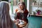 Grey haired woman with glasses looks at friend sitting at small table in cozy cafe