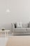 Grey lounge in real photo of bright living room interior with white lamp, carpet and wooden table. Paste your graphic here