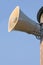 Grey plastic horn loudspeaker on pole post, blue sky, large detailed vertical closeup