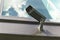 Grey security camera with window reflecting blue sky clouds