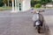Grey small motorcycle parked on the side of a road at the background of blurred gas station with place for your text