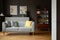 Grey sofa with yellow cushion in vintage living room interior with posters and lamp. Real photo