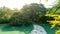 The grey stepping stone curve concrete walkway and a bridge cross a clean lake among greenery trees, shrub and bush in a park