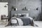 Grey stool in front of bed with blankets and cushions in dark ho