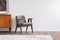 Grey vintage armchair next to retro cabinet with books, warm carpet on wooden fool, real photo