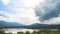 Grey and white clouds float over calm lake against hills