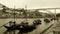 Greyscale panoramic shot of boats in the river with a bridge on the background