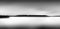 Greyscale panoramic view of a sea under a cloudy sky with a forest behind the fog