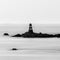 Greyscale shot of a lighthouse in Guernsey surrounded by the water