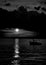 Greyscale shot of a ship in the sea under the dark cloudy sky with the moon in the background