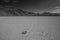 Greyscale shot of stone at the end of a trace surrounded by high rocky hills in Death Valley, USA