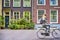 Gril Passing on Conventional Dutch Bicycles Against Classic Red House with Lots of Flowers on the Background. Blurred Motion