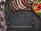Grill or barbecue food background. Empty cast iron grill griddle and meat fork on rustic kitchen table. Various sausages on a