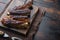 Grilled barbecue pork ribs, on wooden serving board, with barbeque knife and meat fork, on old dark  wooden table background