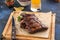 Grilled barbecue spareribs and bbq sauce on wooden board and glass of beer on blue background