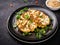 Grilled cauliflower steaks with greens and herbs on black plate, close up. Healthy eating, plant based meat substitute concept.