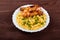 Grilled chicken drumstick and pasta on white plate, brown wooden background