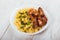 Grilled chicken drumstick and pasta on white plate, wooden background