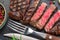 Grilled delicious ribeye steak slices and food utensils on black slate serving plate. Flat lay